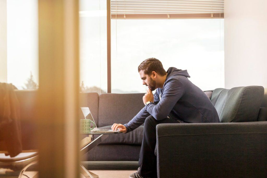 young man focused on laptop in modern, sunlit room, embodying productivity and comfort.