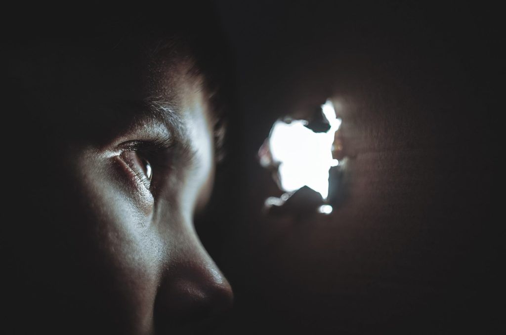 child in darkness gazes at light through hole, filled with wonder and curiosity.