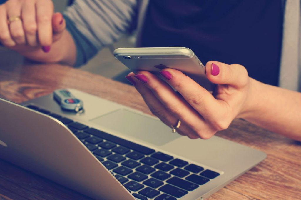 person using smartphone and laptop in stylish and cozy workspace.