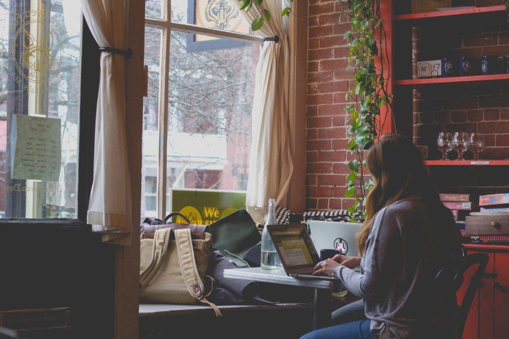 tranquil urban café scene with woman working on laptop, surrounded by natural light and greenery.