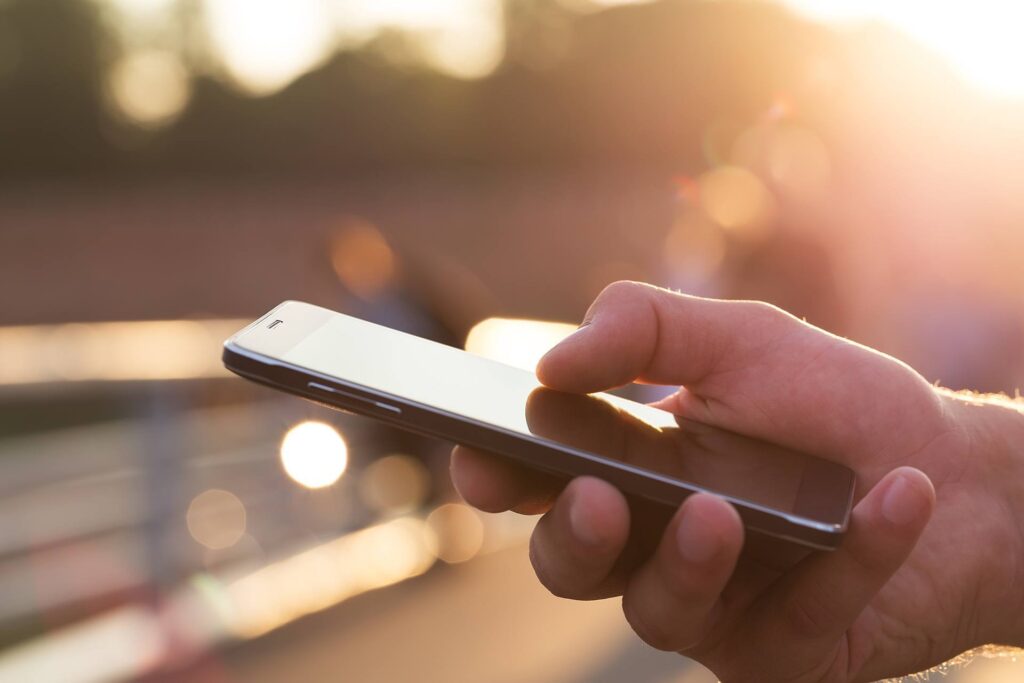 peaceful sunset moment: hand using smartphone outdoors in warm golden light.