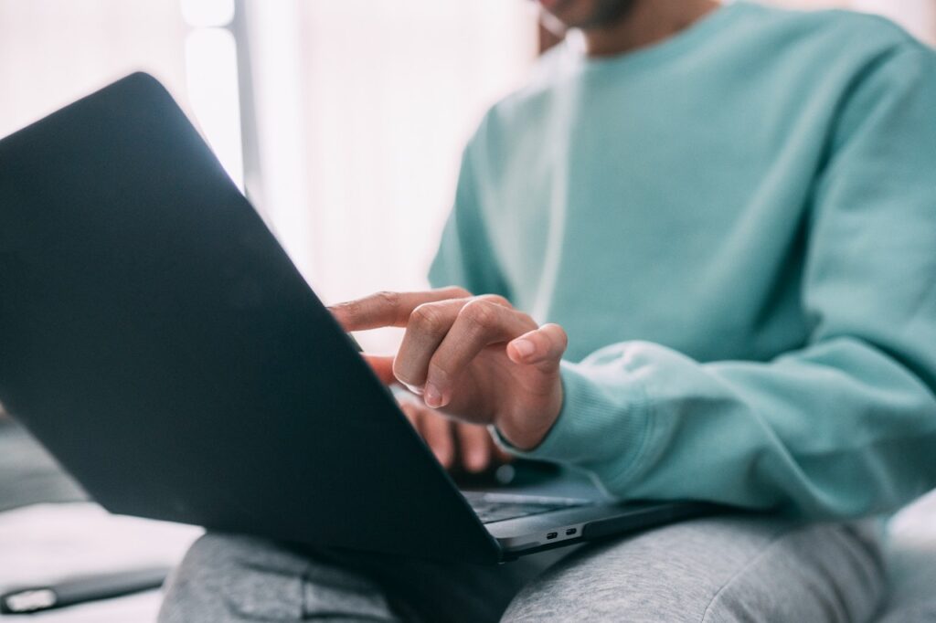 tranquil workspace: person in light blue sweater typing on laptop on cozy couch.