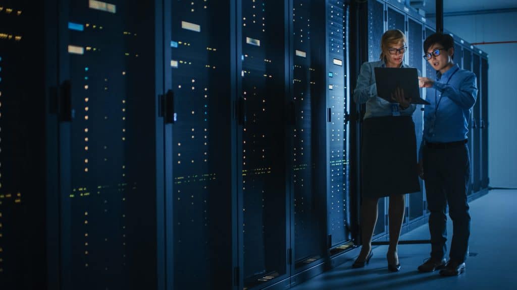 two people in a server room looking at a laptop