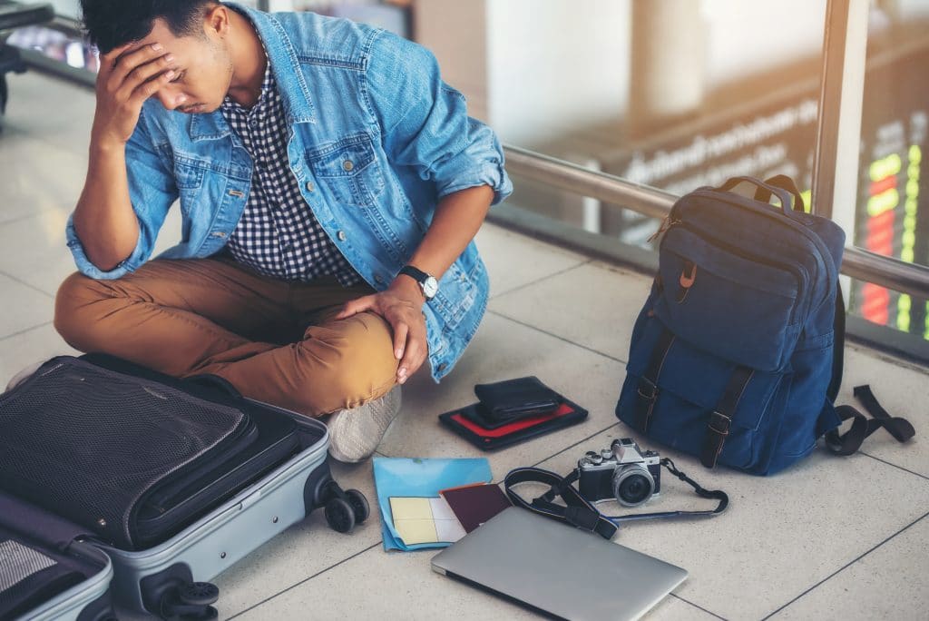 stressed traveler surrounded by belongings in chaotic airport terminal.