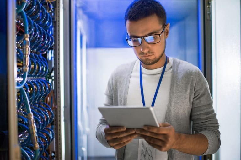 focused it professional managing data center operations with digital tablet in blue-lit server room.