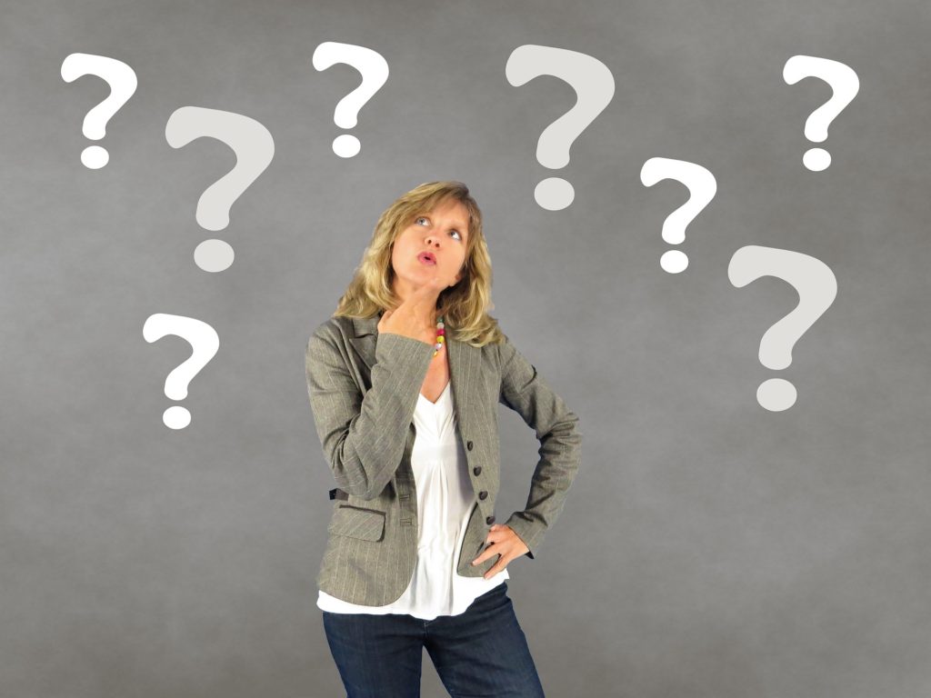 contemplative woman in gray outfit pondering with floating question marks.