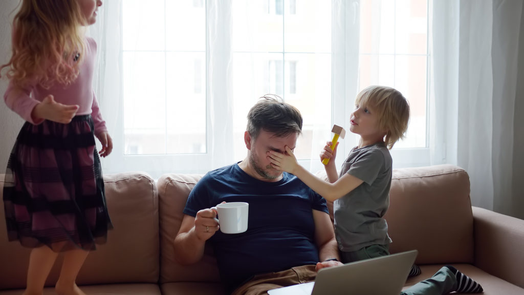 father multitasks work and play with children in cozy living room, showcasing work-life balance.