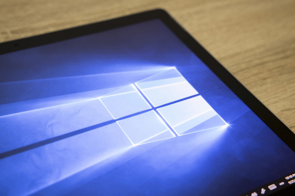 windows 10 interface on blue screen with logo and taskbar, on wooden table.