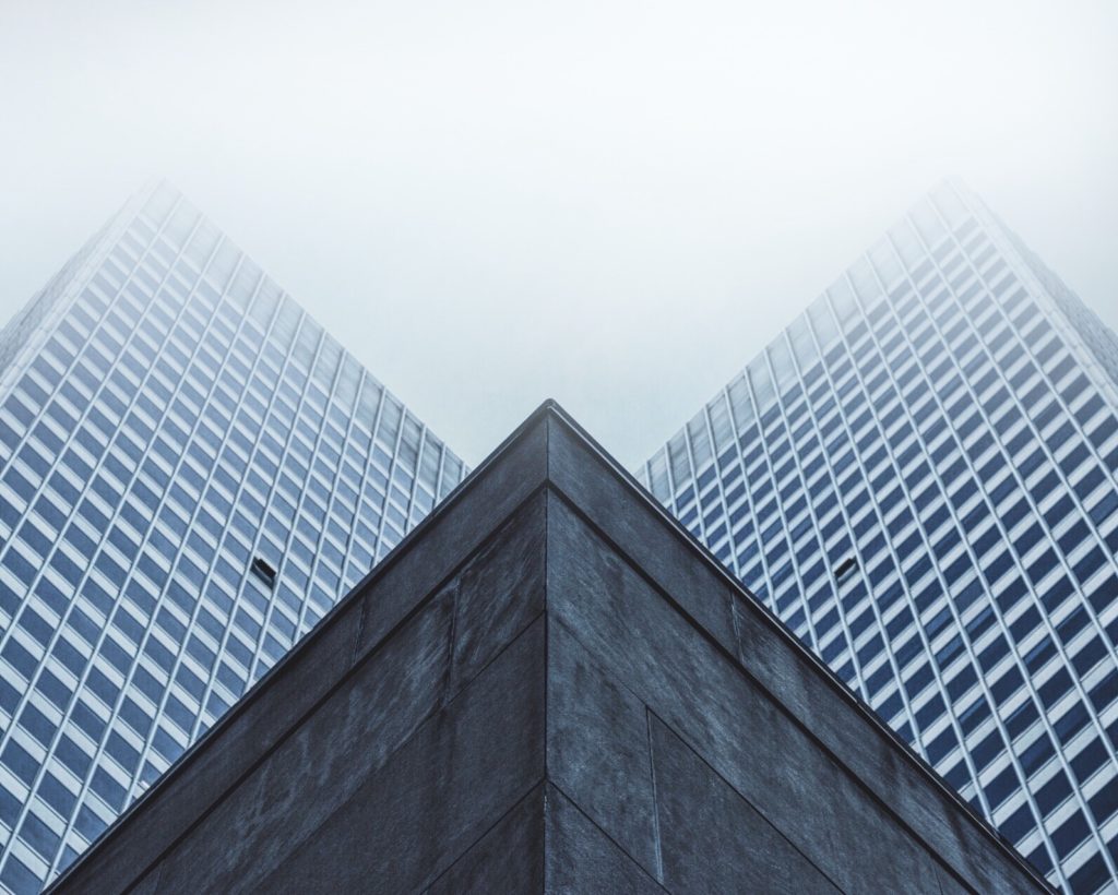 symmetrical glass skyscrapers rise through fog, reflecting light and creating a modern urban elegance.