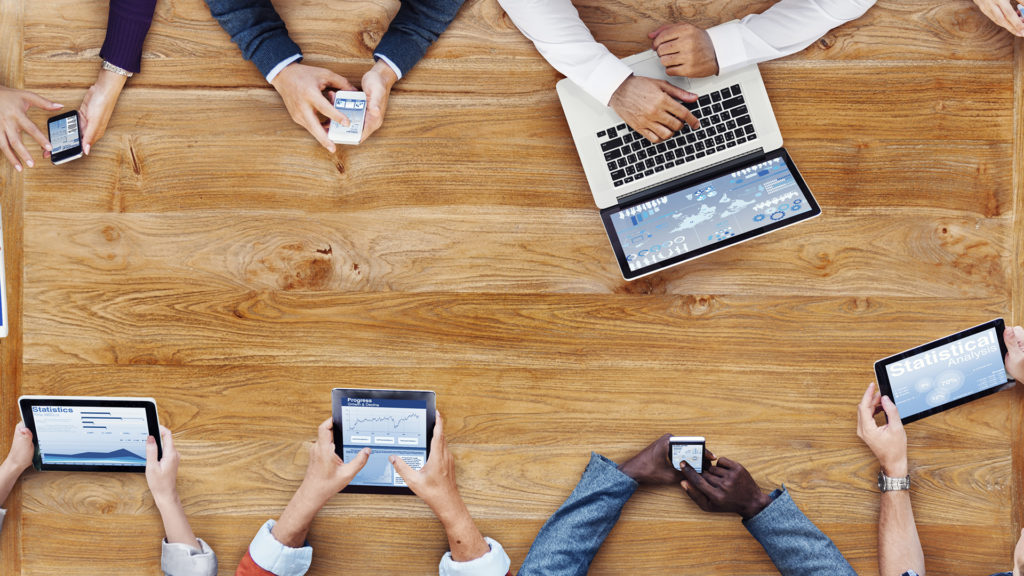 diverse professionals collaborating with laptops, tablets, and smartphones in modern workspace.