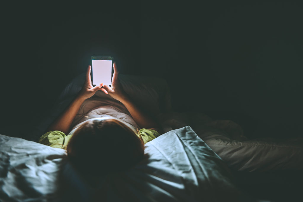 cozy nighttime scene: person in bed engrossed in smartphone glow.