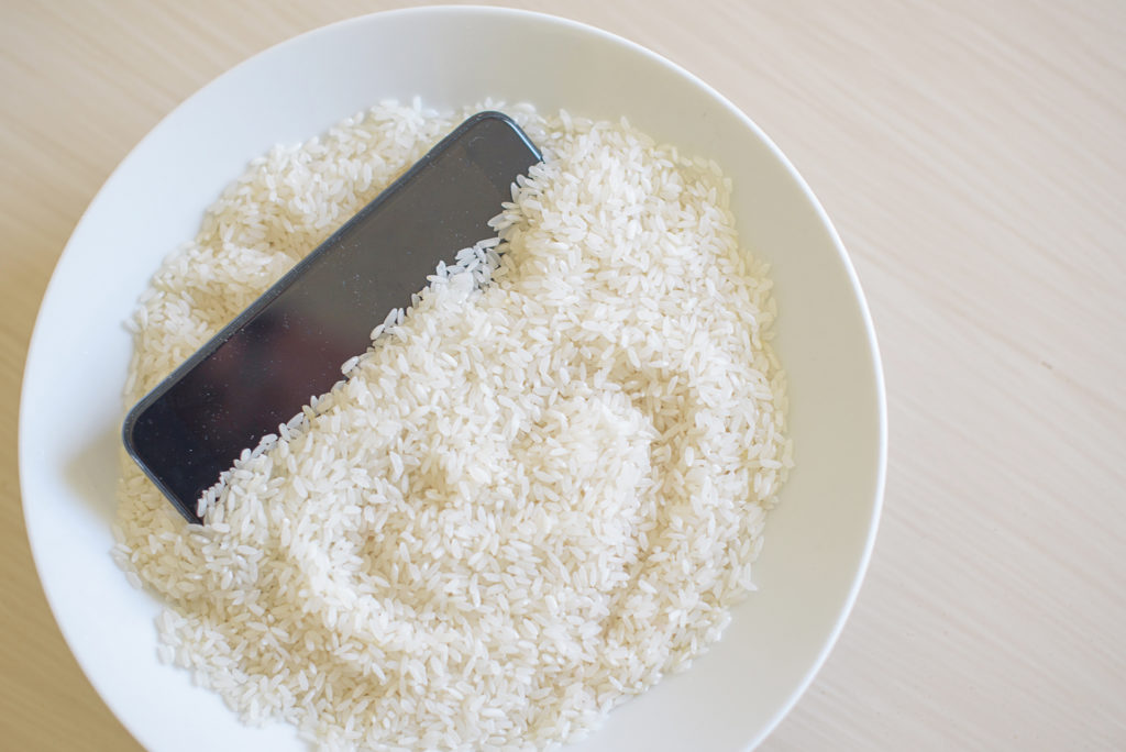 modern technology meets tradition: smartphone nestled in bowl of uncooked white rice.