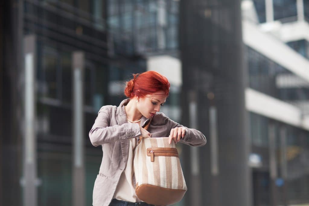 stylish red-haired woman searching bag in modern city environment.