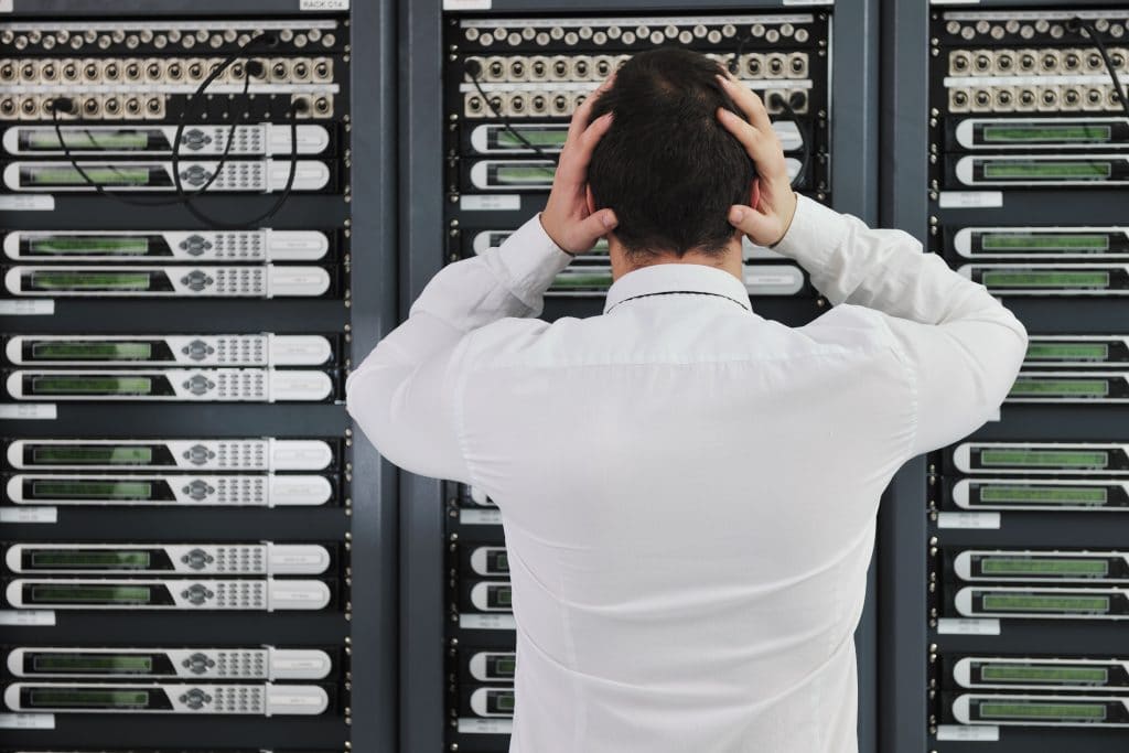 frustrated it worker overwhelmed by complex server equipment in dimly lit room.