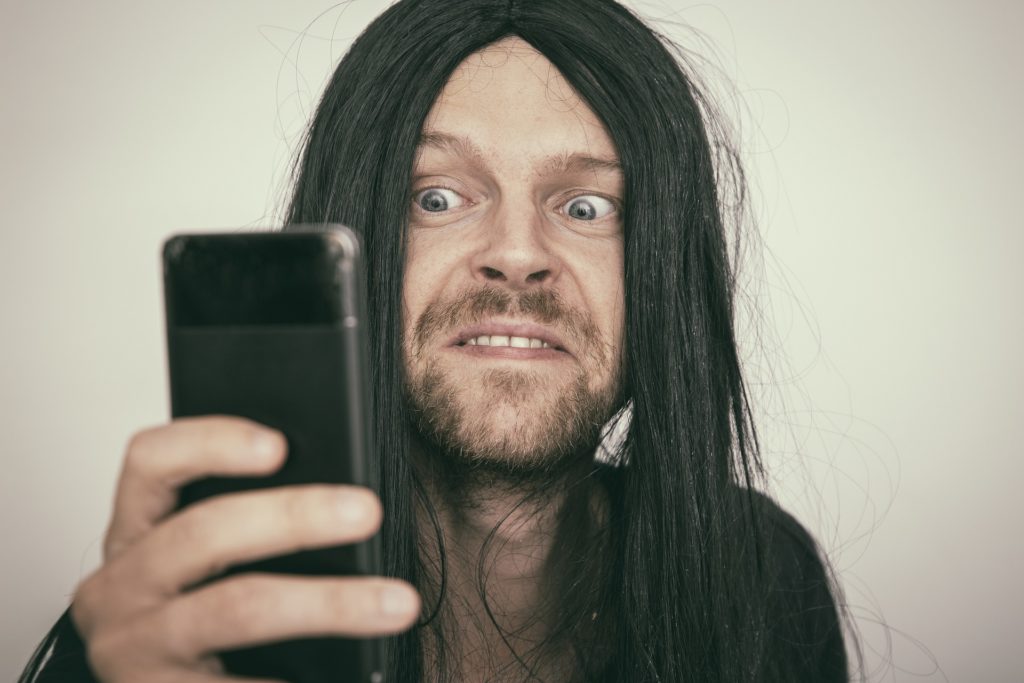 surprised man with long hair reacting to smartphone content.