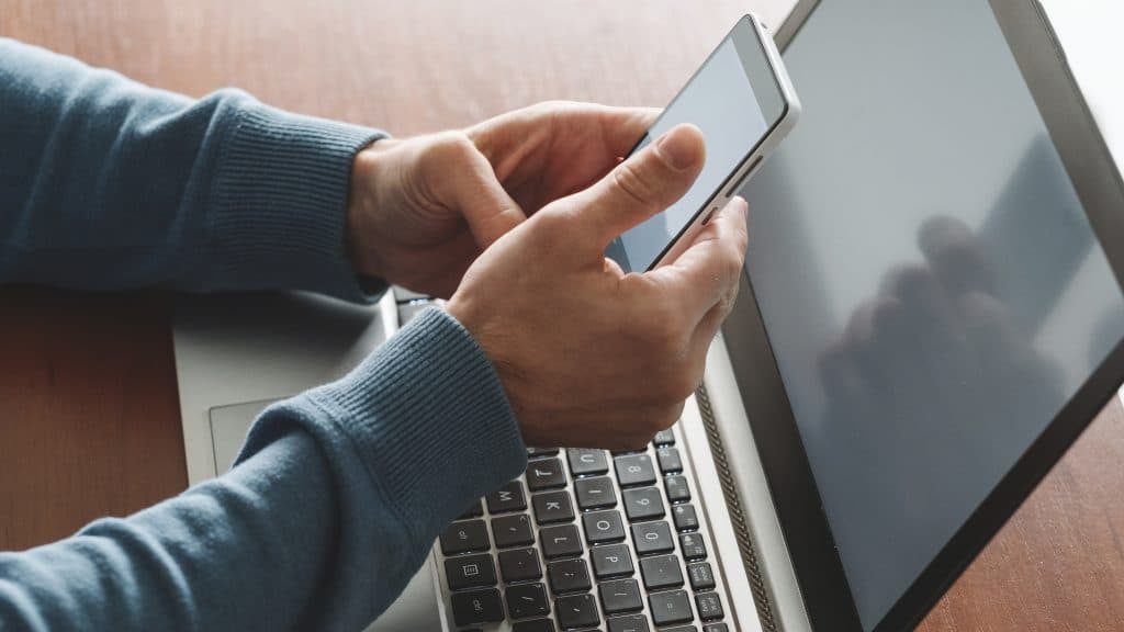 digital multitasking: person using smartphone and laptop in cozy workspace.