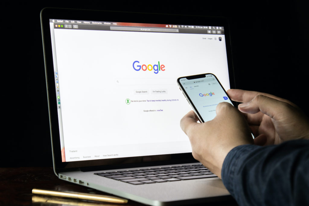 man in bangkok multitasking on smartphone and macbook, interacting with google for information.