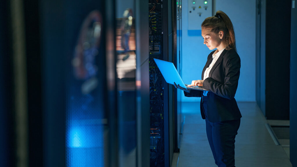 professional woman in data center managing network performance with laptop.