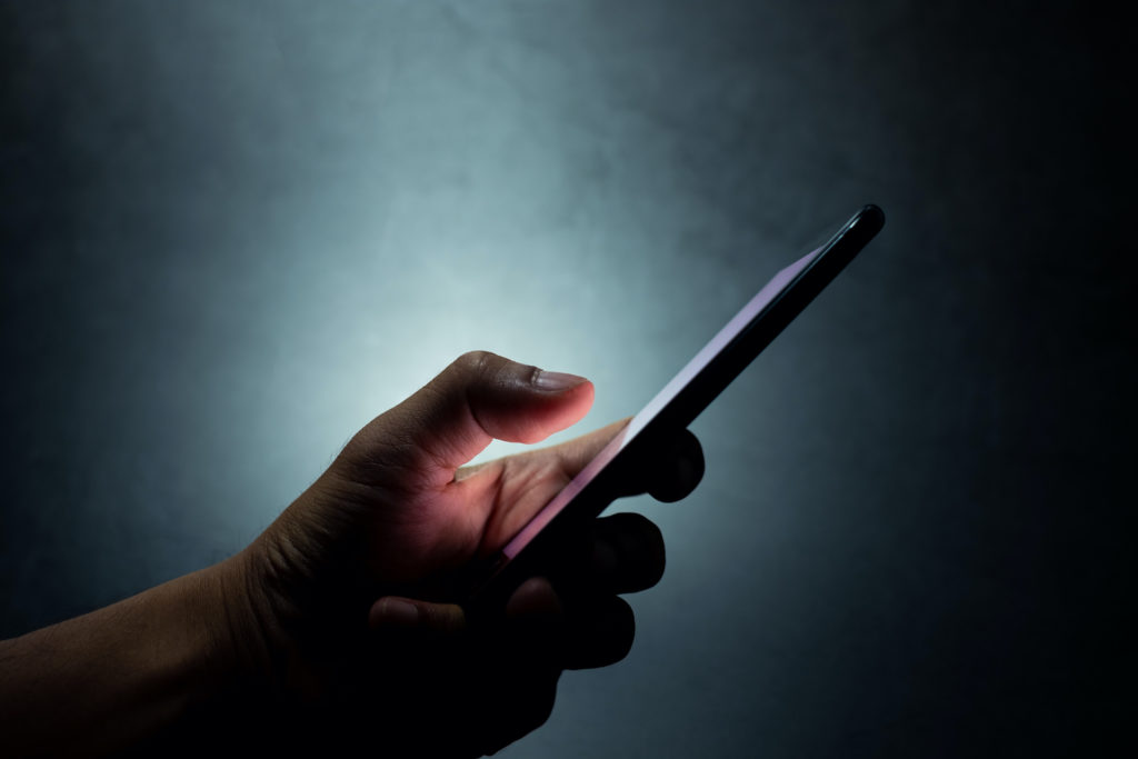 hand touching smartphone screen in dark blue background, symbolizing digital connection and interaction.