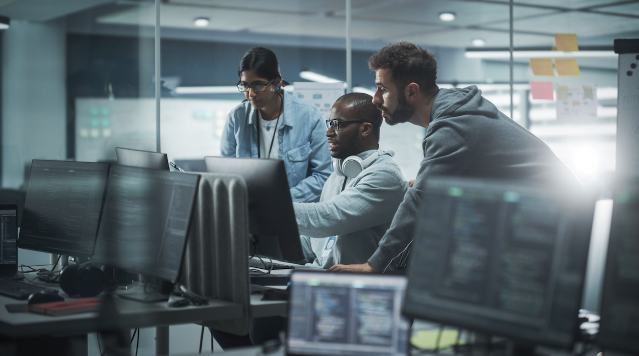 tech team collaboration in modern office with diverse individuals brainstorming on computer screens.