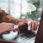 Focused man typing on laptop, managing cloud-based documents in modern office setting.