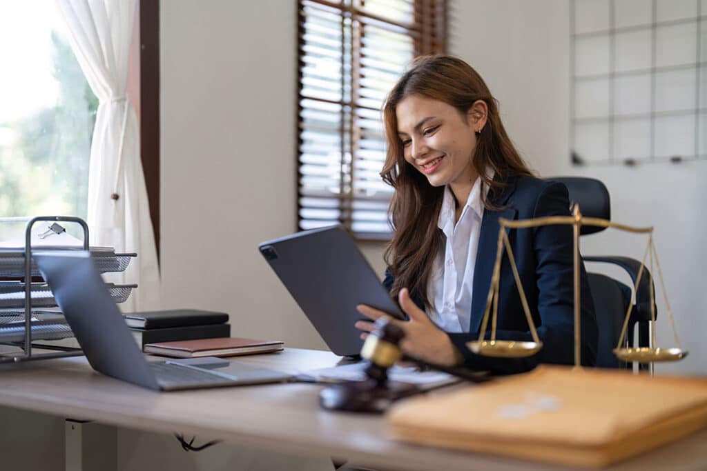 young lawyer reviewing contracts, symbolizing justice with brass scale, at well-organized office desk.