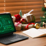 Cozy holiday workspace with secure tablet, open notebook, red mug, and festive Christmas tree.