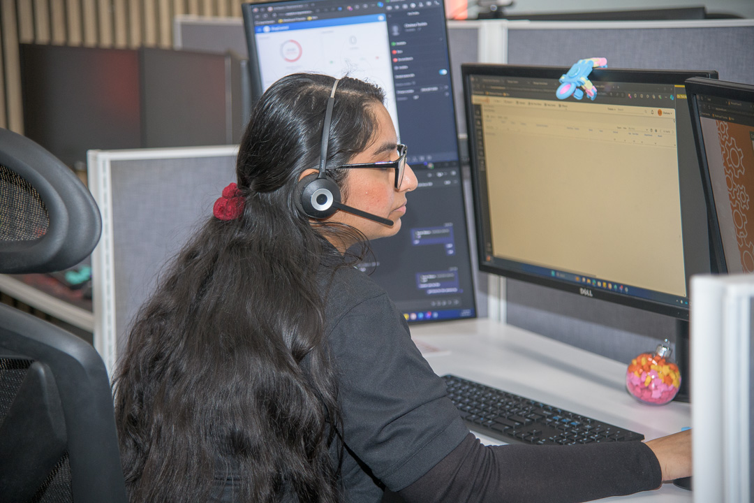 woman working diligently at a modern office desk with dual monitors and headset.