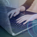 Person typing on laptop keyboard with digital coding background and security shield symbol.