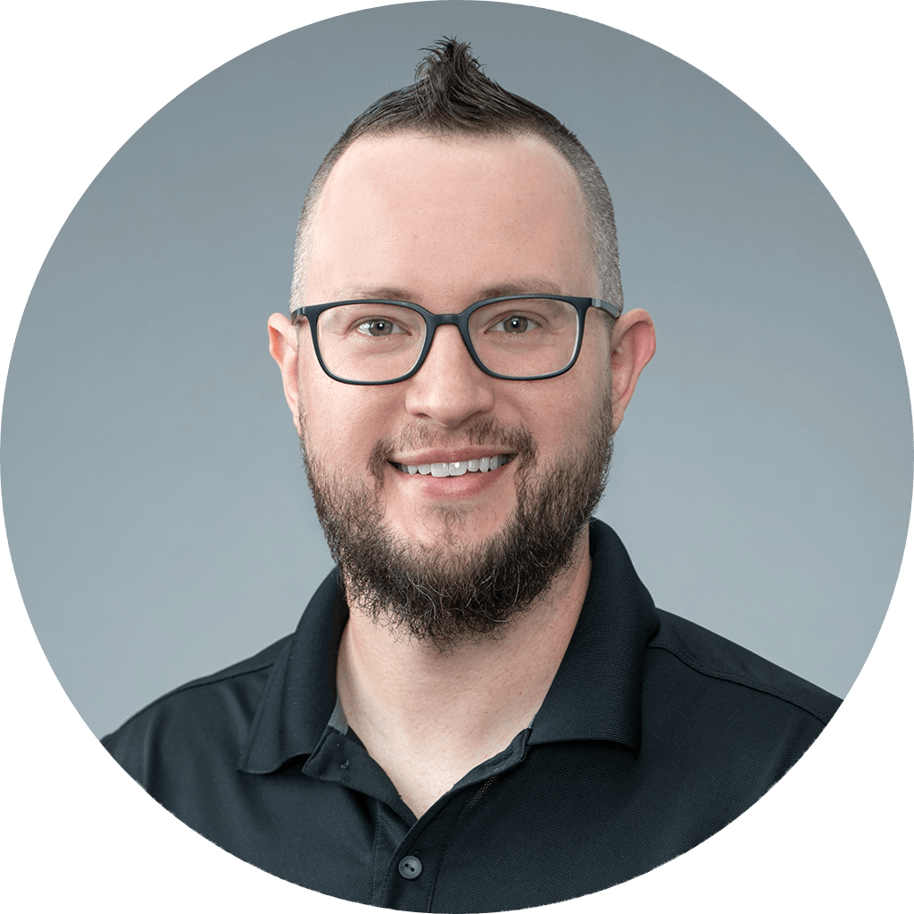 professional portrait of a friendly man with stylish mohawk, beard, and glasses.