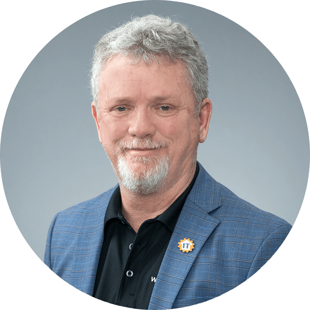 middle-aged man in black polo shirt and blue plaid blazer, with gray goatee.