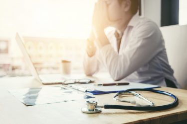 overwhelmed doctor contemplating at desk, surrounded by medical tools and paperwork.