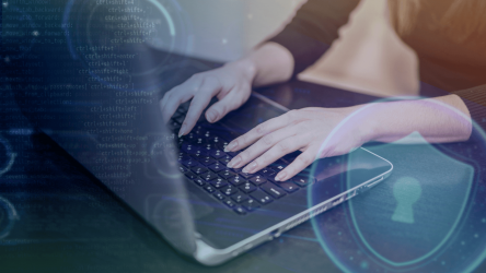 person typing on laptop keyboard with digital coding background and security shield symbol.